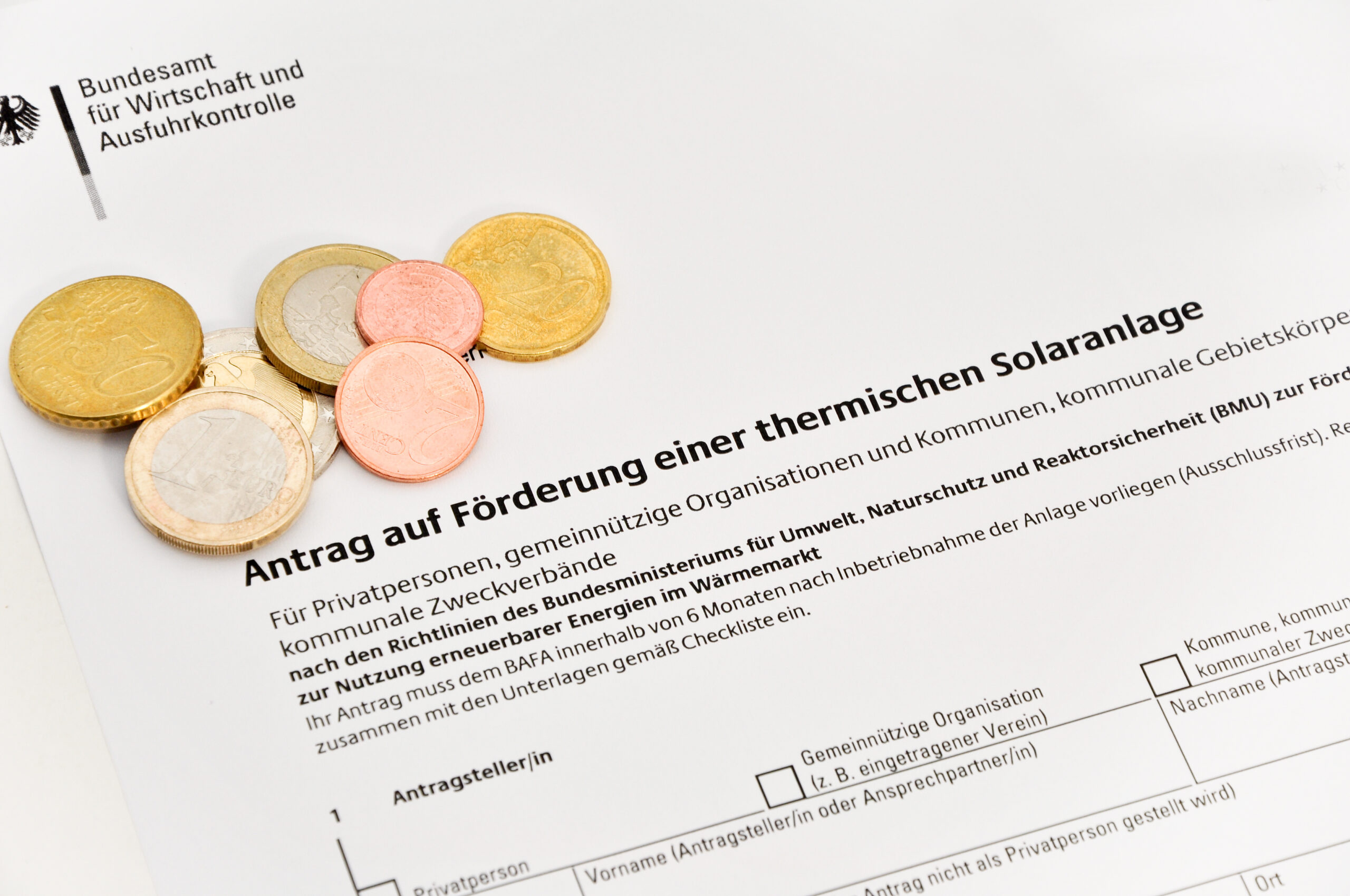 Münzen auf einem Antrag auf Förderung einer thermischen Solaranlage – Thema Förderanträge